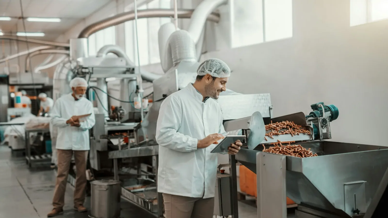 Supervisor reviewing a tablet beside a food production line.